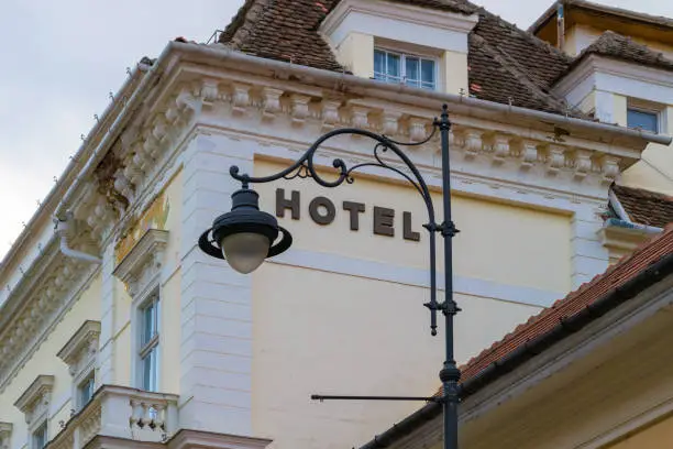 Generic hotel sign framed by an artistically curved street lamp, with renovated old buildings in the background. Concept for travel, accommodation, tourism, holidays - Sibiu, Transylvania, Romania.