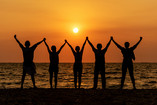 Silhouette of friends and teamwork standing on beach during sunset time for success business.  Lifestyle and Teamwork Concept