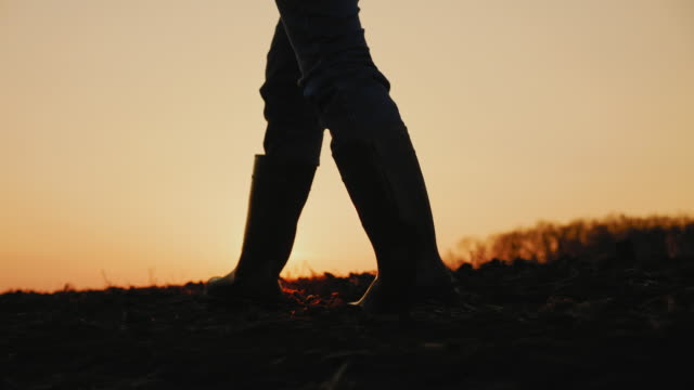 Male farmer in rubber boots walking through cultivated agricultural field