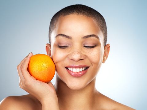 Studio shot of a beautiful young woman posing with an orange against a blue background