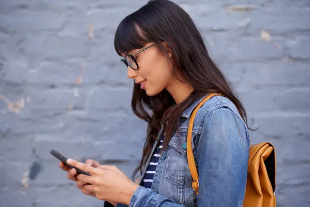 Shot of a young woman texting on a cellphone against a grey wall