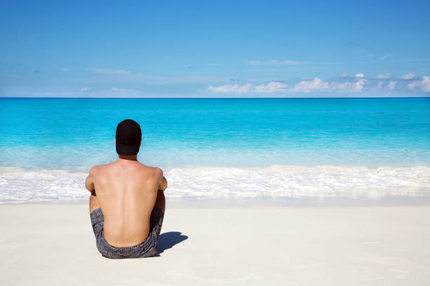 istock Man gazing at the ocean in deep thought while sitting on the beach. 1139913796