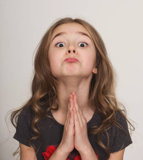 Little girl pleading with hands clasped together Oh please, may I please. Cute little girl pleading with hands clasped together, with funny grimace pleading stock pictures, royalty-free photos & images