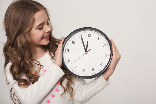 Learning to tell time. Cute little girl holding big clock on white background, copy space