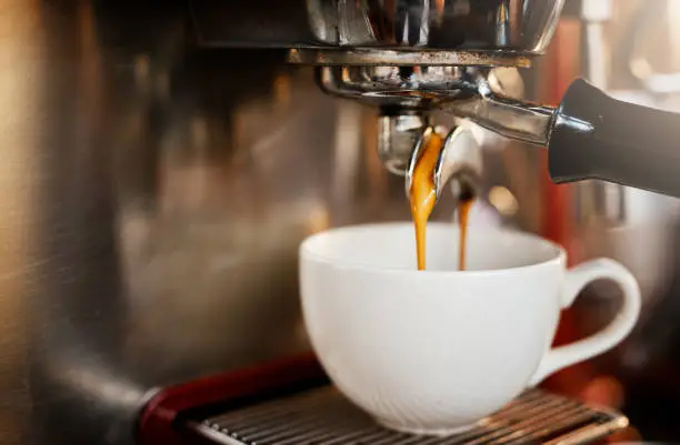 Closeup shot of an espresso maker pouring coffee into a cup inside of a cafe