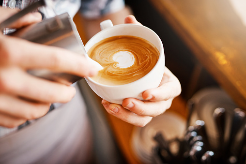 A cropped shot of an unrecognizable barista pouring frothy milk into a cup of hot coffee turning it into a picture