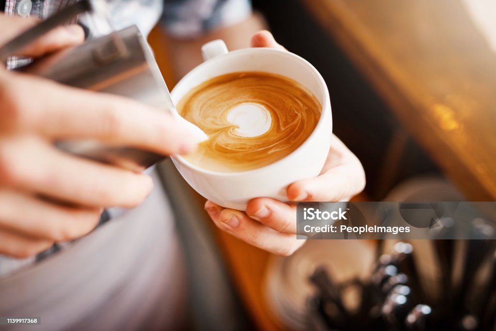 Making pictures A cropped shot of an unrecognizable barista pouring frothy milk into a cup of hot coffee turning it into a picture Cafe Stock Photo