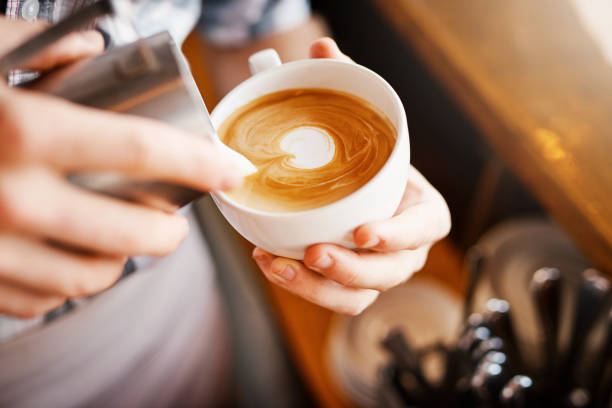 Making pictures A cropped shot of an unrecognizable barista pouring frothy milk into a cup of hot coffee turning it into a picture serving food and drinks photos stock pictures, royalty-free photos & images
