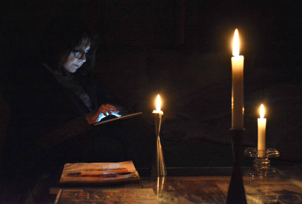 Lifestyle, " Power Failure, Reading by Candlelight " Lifestyle...This moody, dark, image shows a woman reading by candle light on her digital tablet, while awaiting the return of power to her home, after a widespread power outage. blackout photos stock pictures, royalty-free photos & images