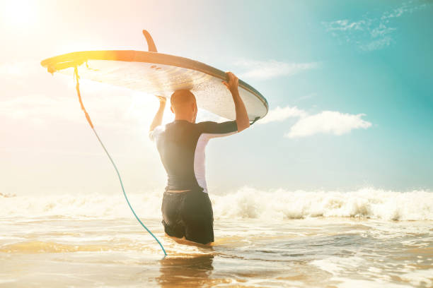 istock Young man Surfer taking surfboard on head and comming with long surf board to waves. Active holidays spending concept. 1139917842