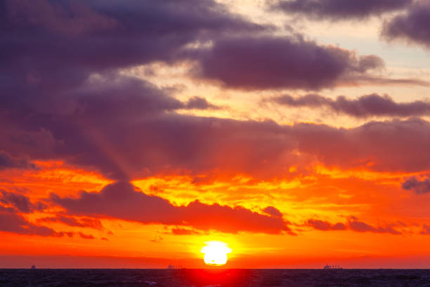 bright orange sun in a cloudy sky over the sea during sunset