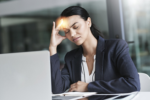 Shot of a young businesswoman suffering with a headache while working in an office