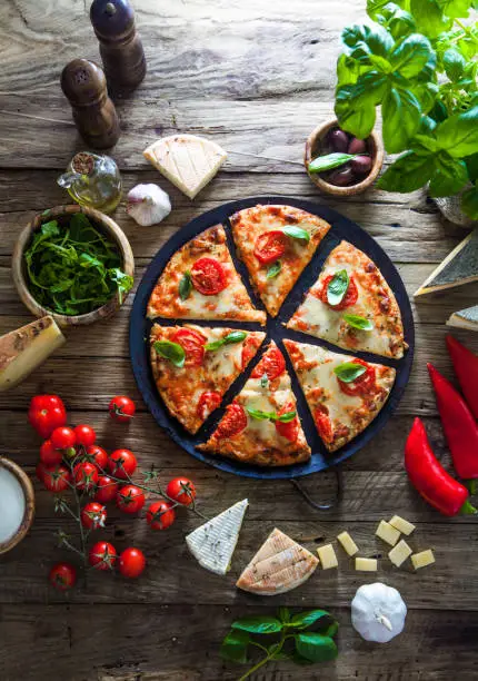 Pizza on wood with ingredients. Pizza with cheese, tomatoes and basil. Rustic italian pizza