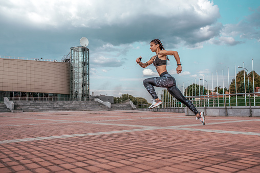 Woman jump athlete girl headphones with phone listens music, while jogging summer city, sportswear leggings top. Free space. Concept healthy lifestyle motivation. Emotions confidence strength speed.