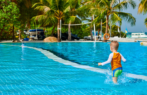 Three year old toddler boy in resort swimming pool. Summer family vacation at Maldives.