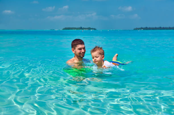 Three year old toddler boy learns to swim with father. Summer family vacation at Maldives.