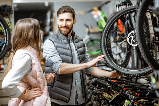 Salesman helping young woman to choose a new bicycle to buy standing in the bicycle shop