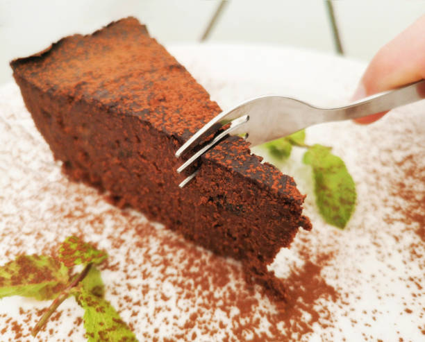 POV of man eating a vegan chocolate cake slice decorated with caco powder and mint
