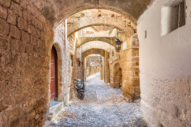 A scooter is parked in an ancient alley with row of homes in old town Rhodes, Greece.