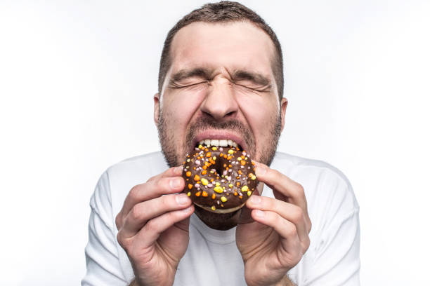 istock This guy is starving so he is eating a big fat chocolate donut. He has closed his eyes and enjoying the moment. Ypoung man likes to eat different kind of sweets. Isolated on white background. 1139945980