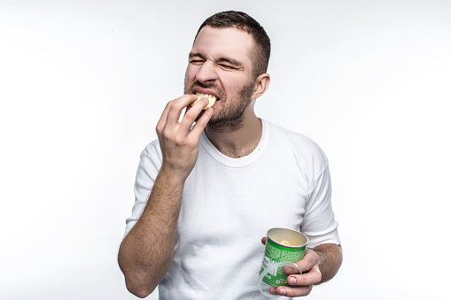 A picture of young nd weird man eating chips from the jar. This food is not healthy and good but he likes it. He is full of joy when he eats junk food. Isolated on white background