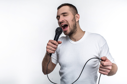 Emotional man is singing song in microphone and rocking out. He is enjoying doing that. Isolated on white background