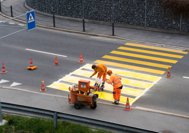 workers painting and marking a pedestrian crosswalk with fresh yellow paint to ensure road and pedestrian safety Maienfeld, GR / Switzerland - April 2, 2019: workers painting and marking a pedestrian crosswalk with fresh yellow paint to ensure road and pedestrian safety freshly painted road markings stock pictures, royalty-free photos & images