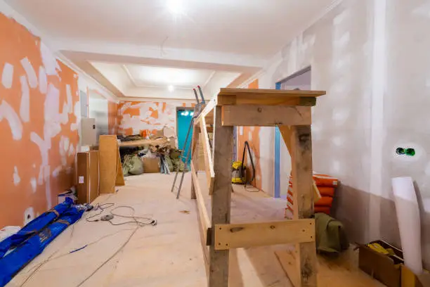 Working process of renovate room from wooden platform, electrical cables and construction materials  in  apartment is under construction, remodeling, renovation, extension, restoration and reconstruction. Paperhangings is measured by tape-measure on the floor and cut. Concept of home improvement