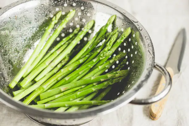 Washed asparagus in a metal colander on a kitchen table. Preparation vegetarian healthy food.