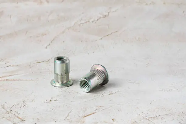 Two metal grey river nuts for hard internal thread for thin units, on left part of oblong horizontal shot textured cement background with copy space for design