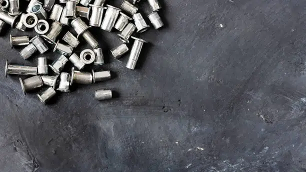 Many metal grey river nuts for hard internal thread for thin units on the upper left part of oblong horizontal, top view on background of black grounge rustic surface with copy space