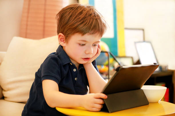 istock Child using tablet pc on bed at home. Cute boy on sofa is watching cartoon, playing games and learning from laptop. Education, fun, leisure, happiness, modern computer technology and communication. 1139985473