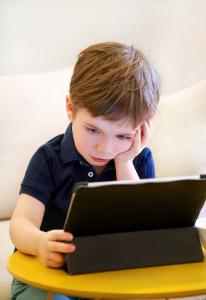 istock Child using tablet pc on bed at home. Cute boy on sofa is watching cartoon, playing games and learning from laptop. Education, fun, leisure, happiness, modern computer technology and communication. 1139985475