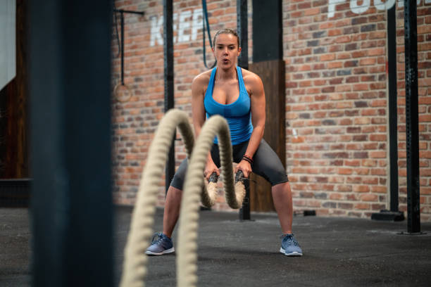 Athletic young woman battle rope training at the gym looking focused
