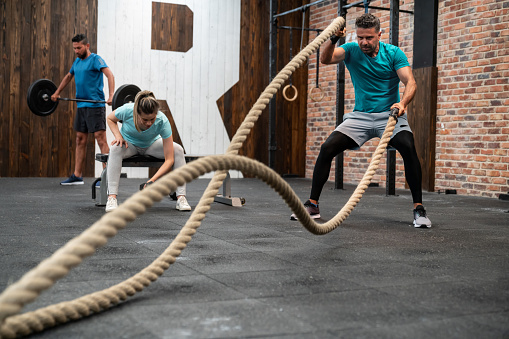 Handsome latin american man training with a battle rope at the gym - Incidnetal people at background