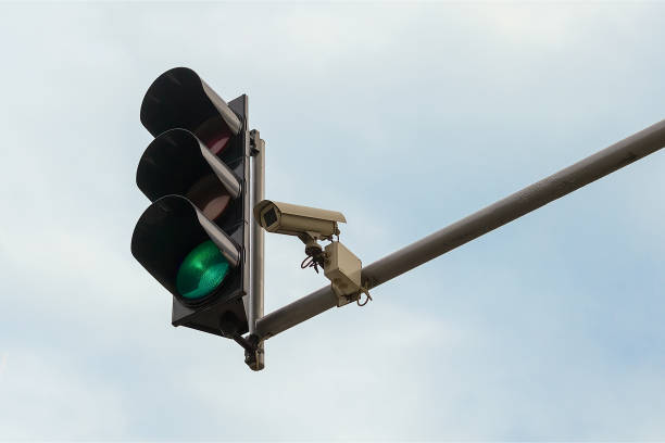 Outdoor surveillance camera and green traffic light both installed on a pole above a roadway, against a blue sky. Modern automatic traffic control. stock photo