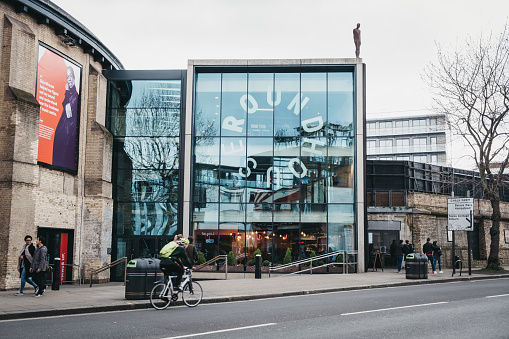 London, UK - March 23, 2019: Cyclist and people in front of The Roundhouse, a performing arts and concert venue situated at the Grade II listed former railway engine shed in Chalk Farm, London, UK.