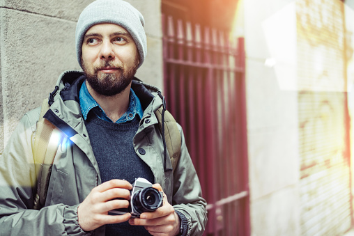 Male casually dressed bearded tourist with a backpack walking through the old town street with retro film photo camera. Traveling and freelance concept.