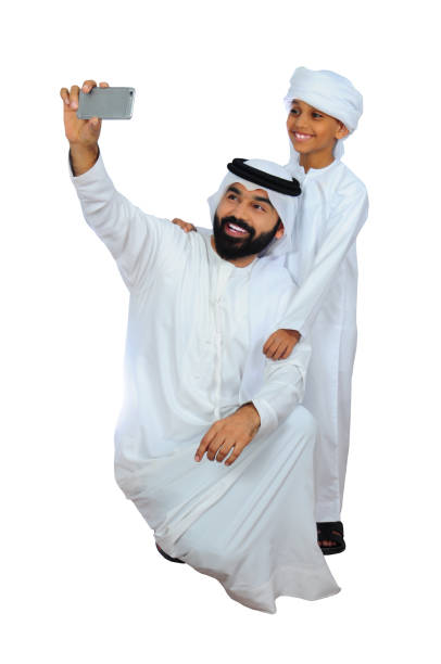 retrato do pai e do filho felizes no vestido tradicional de emirati (tomando a tecnologia do selfie) - saudi arabia child ramadan offspring - fotografias e filmes do acervo