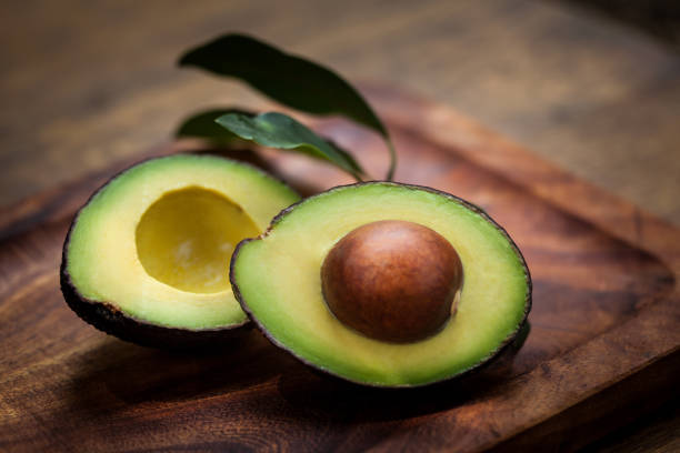 moitié d’avocat sur une planche en bois - avocat légume photos et images de collection