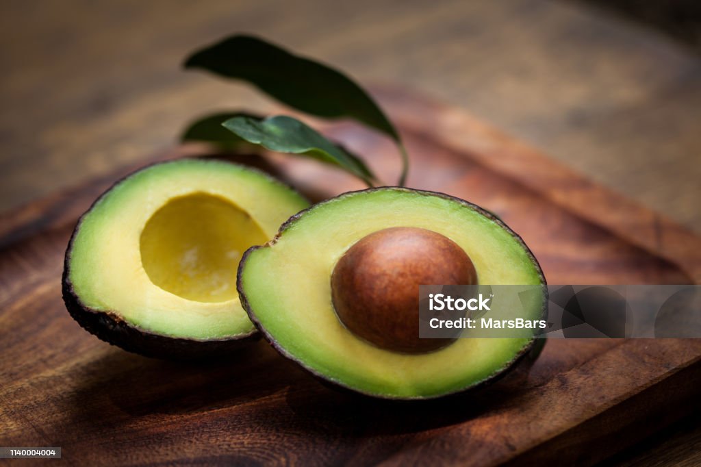 Avocado halves on a wooden board Avocado Halves on a wooden board with avocado leaves Avocado Stock Photo