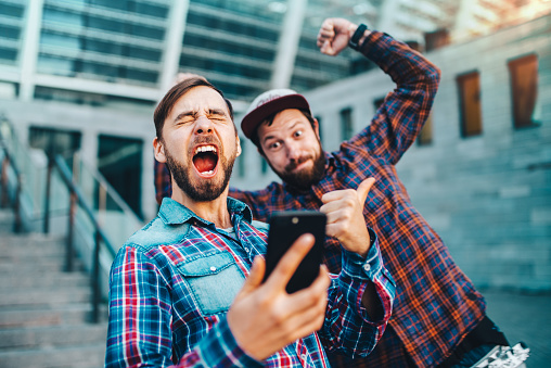 Two friends showing sincere emotions of joy about victory in online lottery. Men being happy winning a bet in online sport gambling application with football stadium on the background.