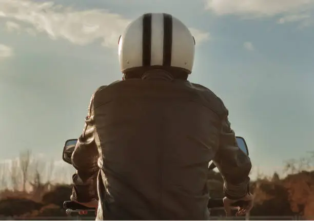 Photo of Man riding motorbike with brown leather jacket and helmet