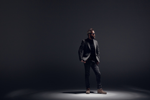 Confident handsome man wearing the jacket standing in the dark room. Horizontal studio shot.