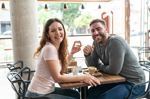 Beautiful couple at a cafeteria enjoying a breakfast while facing camera smiling very happy