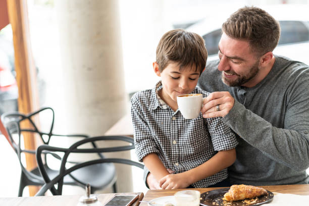istock Loving father with his son sitting on lap sharing his warm drink while both smiling at a bakery 1140019898