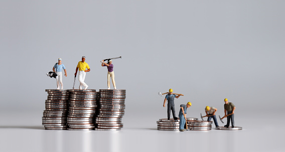 Miniature people standing on a pile of coins. A concept of income disparity.