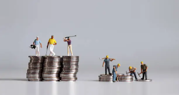 Photo of Miniature people standing on a pile of coins. A concept of income disparity.