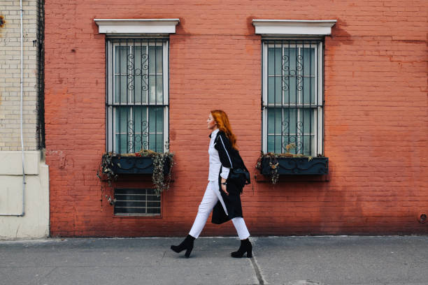 Fashionable redhead woman walking by the brick wall building in West Village, Manhattan, NY Vintage toned portrait of a young redhead New Yorker woman, walking on a nice and sunny spring day by the old, brick wall buildings in West Village, in Lower Manhattan area. She is wearing casual but stylish clothes, enjoying her day. wall sidewalk city walking stock pictures, royalty-free photos & images