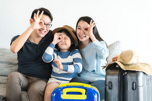 exited asian family mom dad daughter happiness trip travel concept with hand pose with luggage on sofa home background